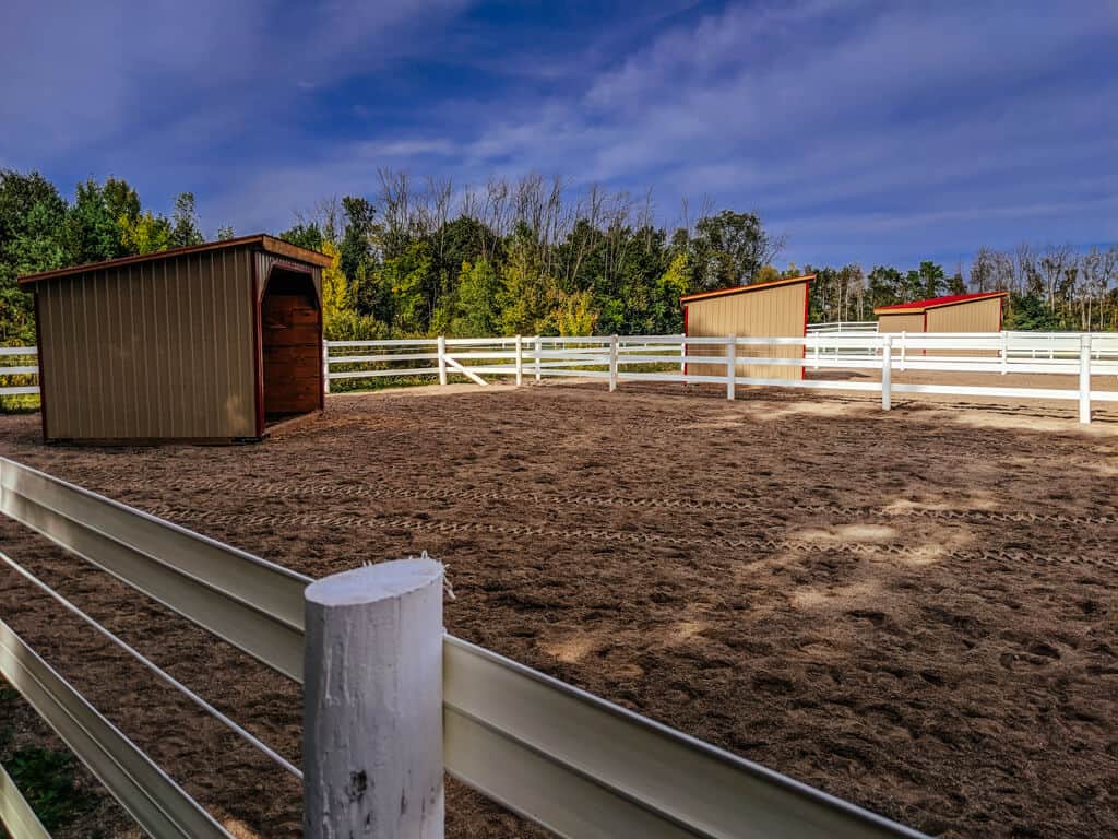 A Horse Barn With Two White Fences And A Dirt Area