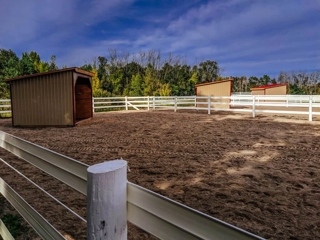 a horse barn with two white fences and a dirt area