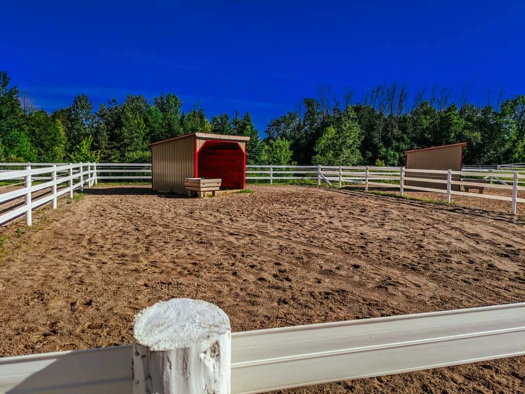 a horse barn with a fence and a red door