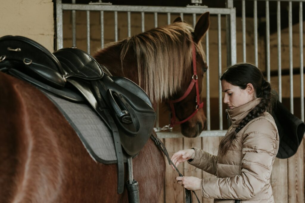 Woman putting saddle on horse